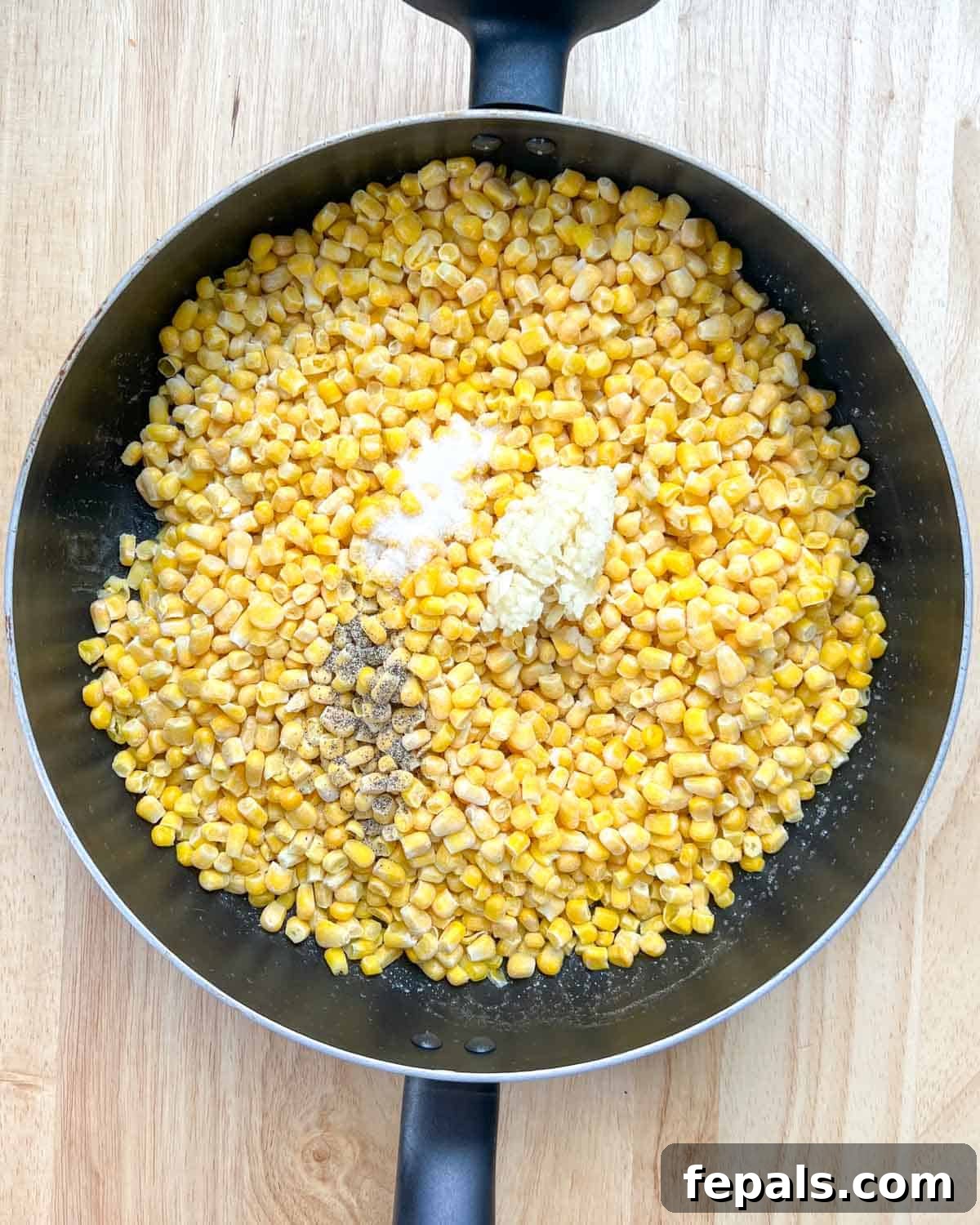 Velvety One-Pot Cheesy Corn 4 Corn kernels being added to a hot skillet where butter has already melted, seasoned with salt, pepper, and minced garlic.