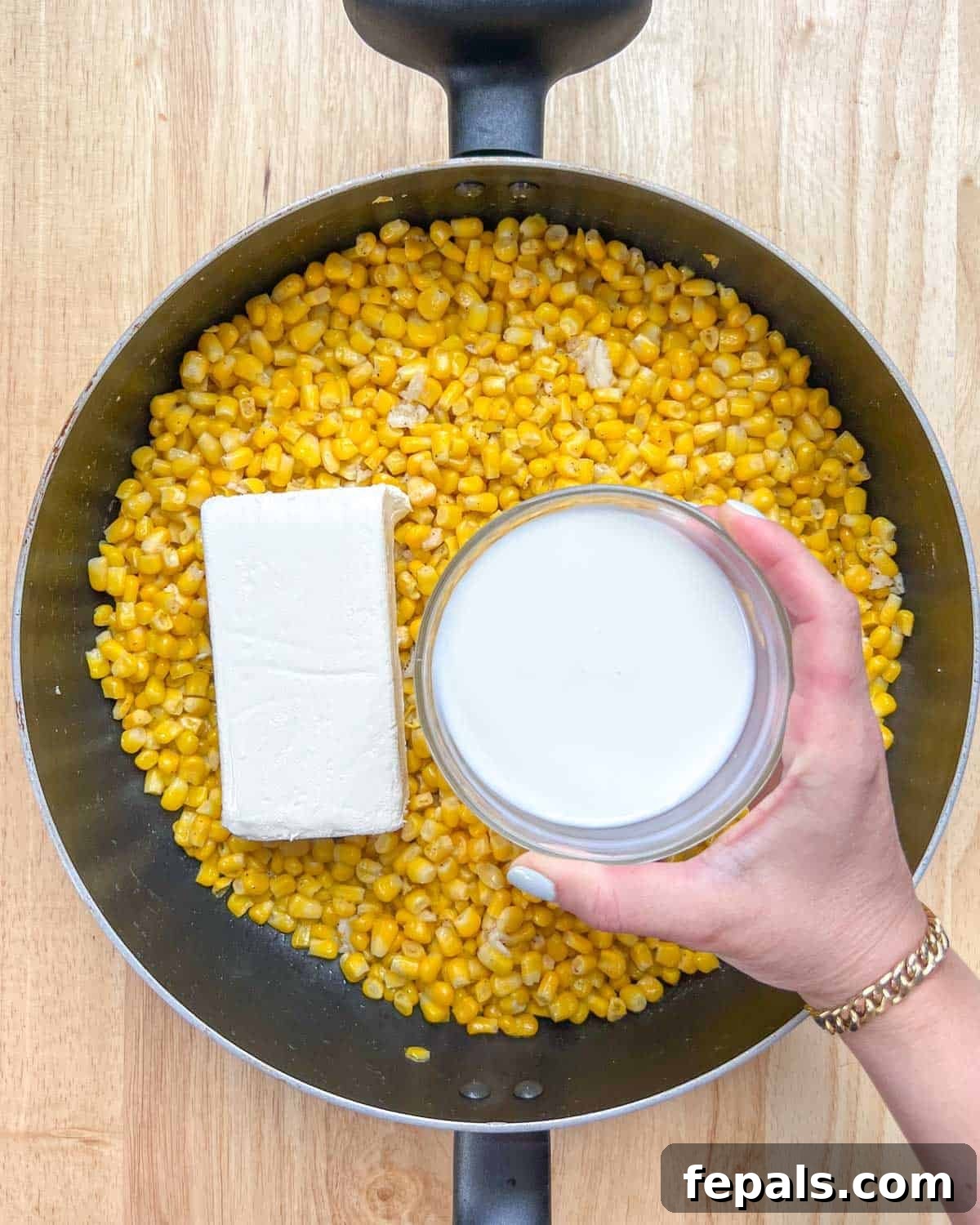 Velvety One-Pot Cheesy Corn 6 Cubed cream cheese and milk being poured over the sautéed corn in the pan, ready to be stirred into a creamy sauce.