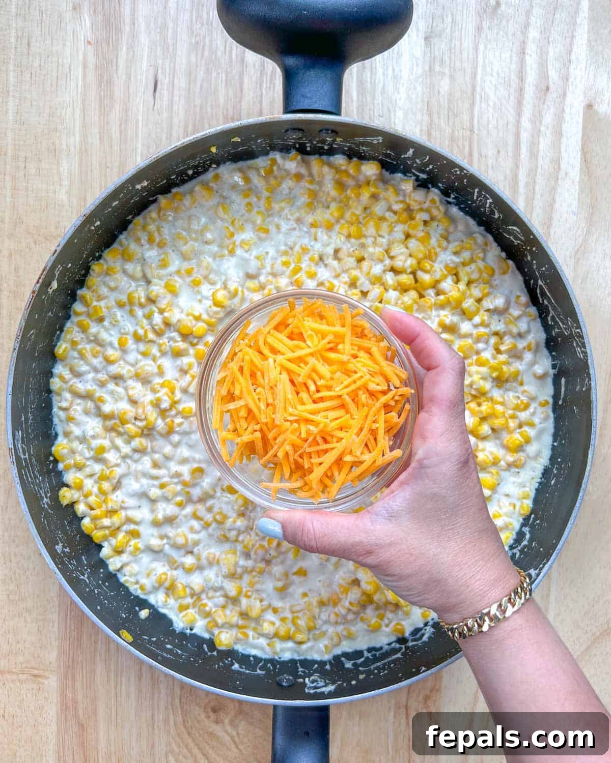 Velvety One-Pot Cheesy Corn 7 Shredded cheddar cheese being generously sprinkled over the simmering cheesy corn, ready to melt into gooey perfection.