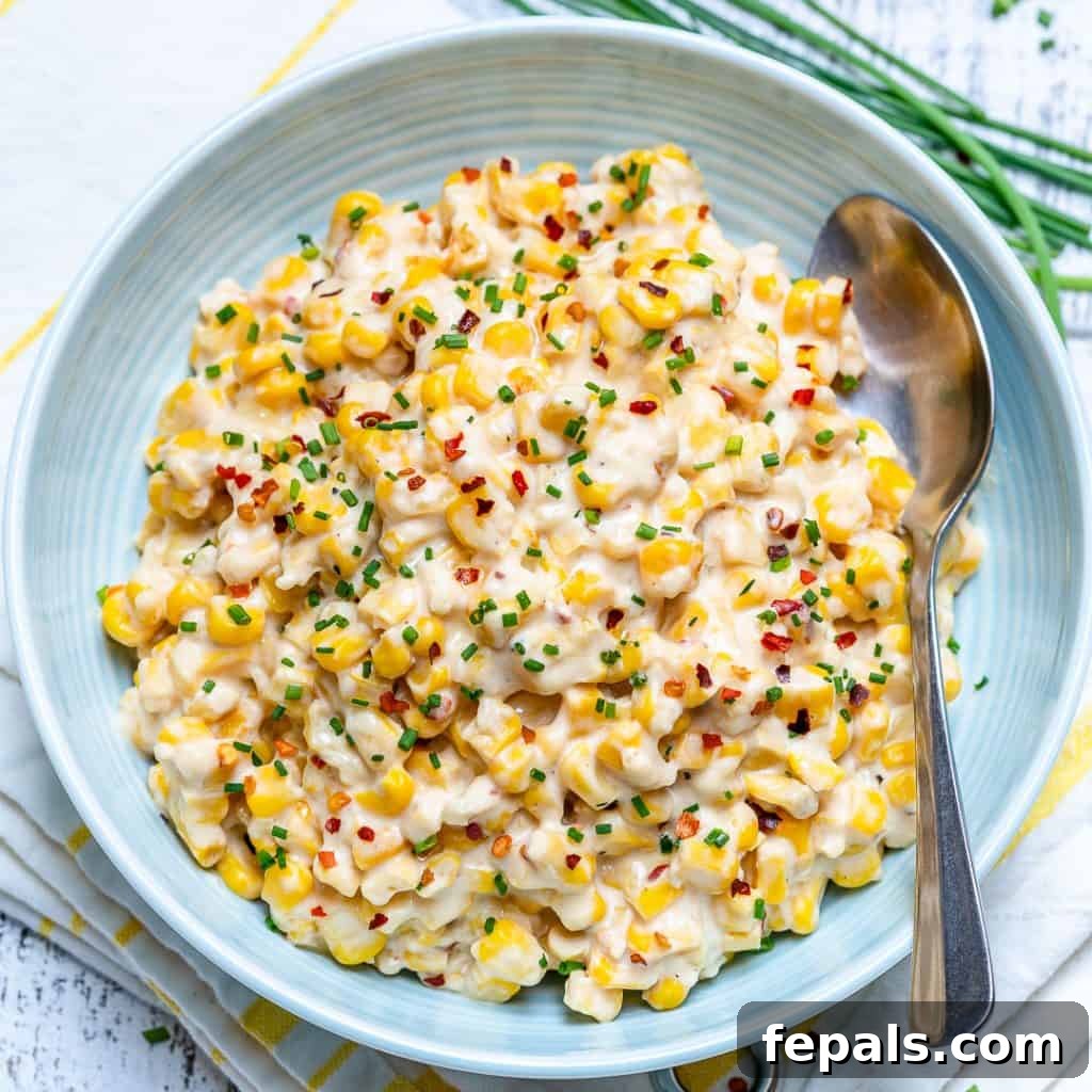 Velvety One-Pot Cheesy Corn 8 Top-down view of a round white plate filled with hot cheesy creamed corn, beautifully topped with red chili flakes and vibrant green chives, with a serving spoon resting to the side.