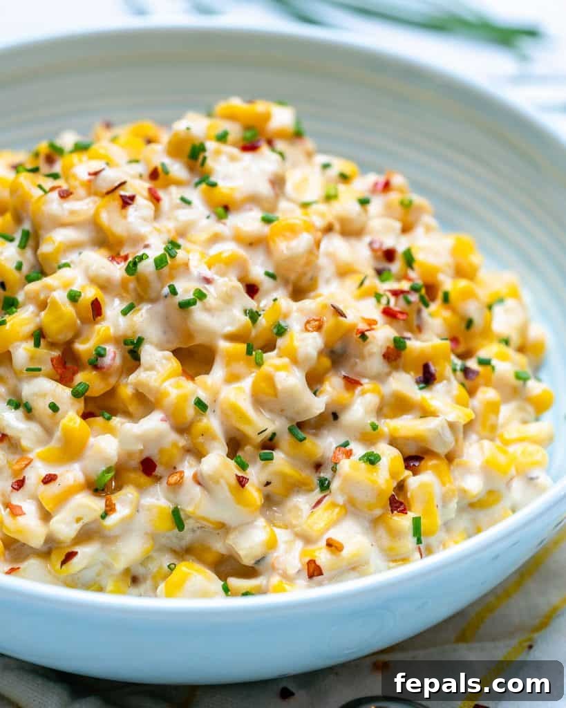 Velvety One-Pot Cheesy Corn 10 A close-up side shot of a plate of Creamed Corn, highlighting its rich, cheesy texture, garnished with chopped chives and a hint of red chili flakes.
