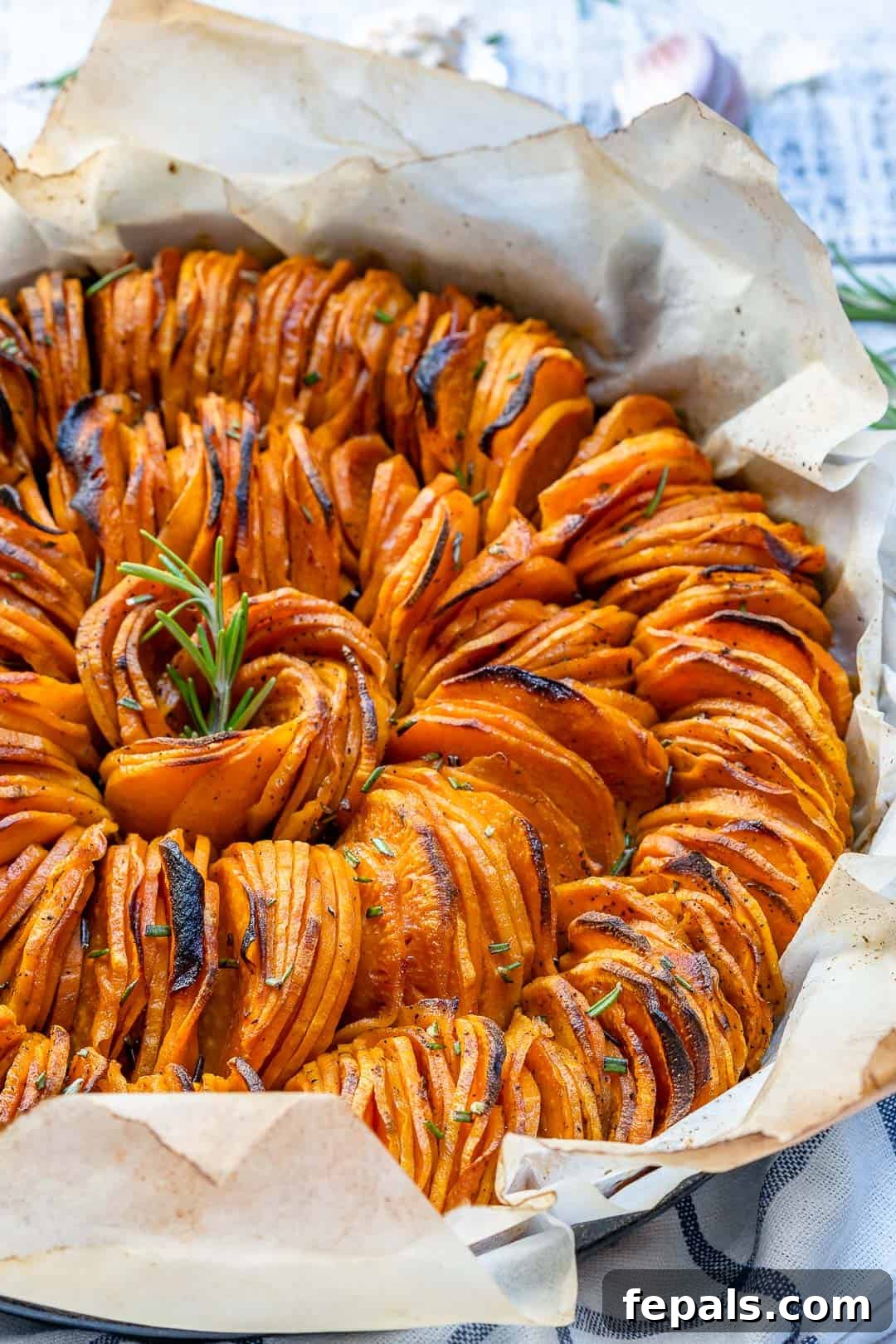 sliced roasted sweet potatoes on parchment paper in a dish garnished with fresh rosemary.