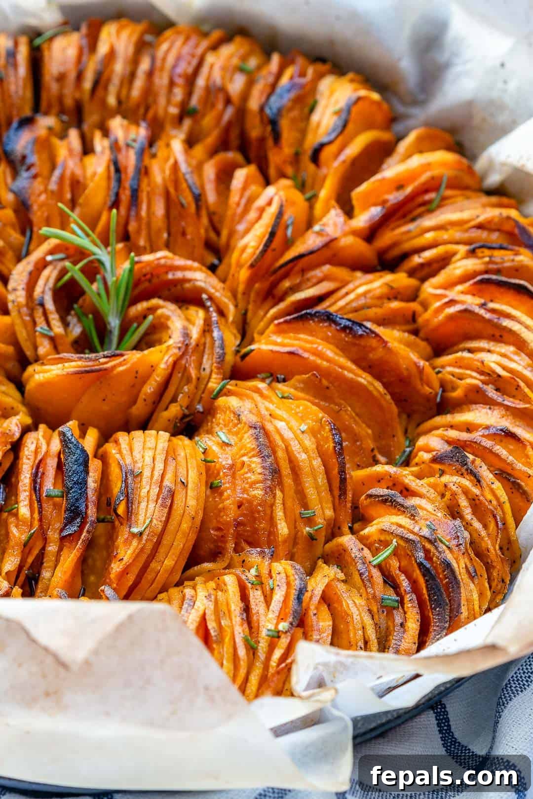sliced baked sweet potatoes lined up in dish with rosemary garnish.