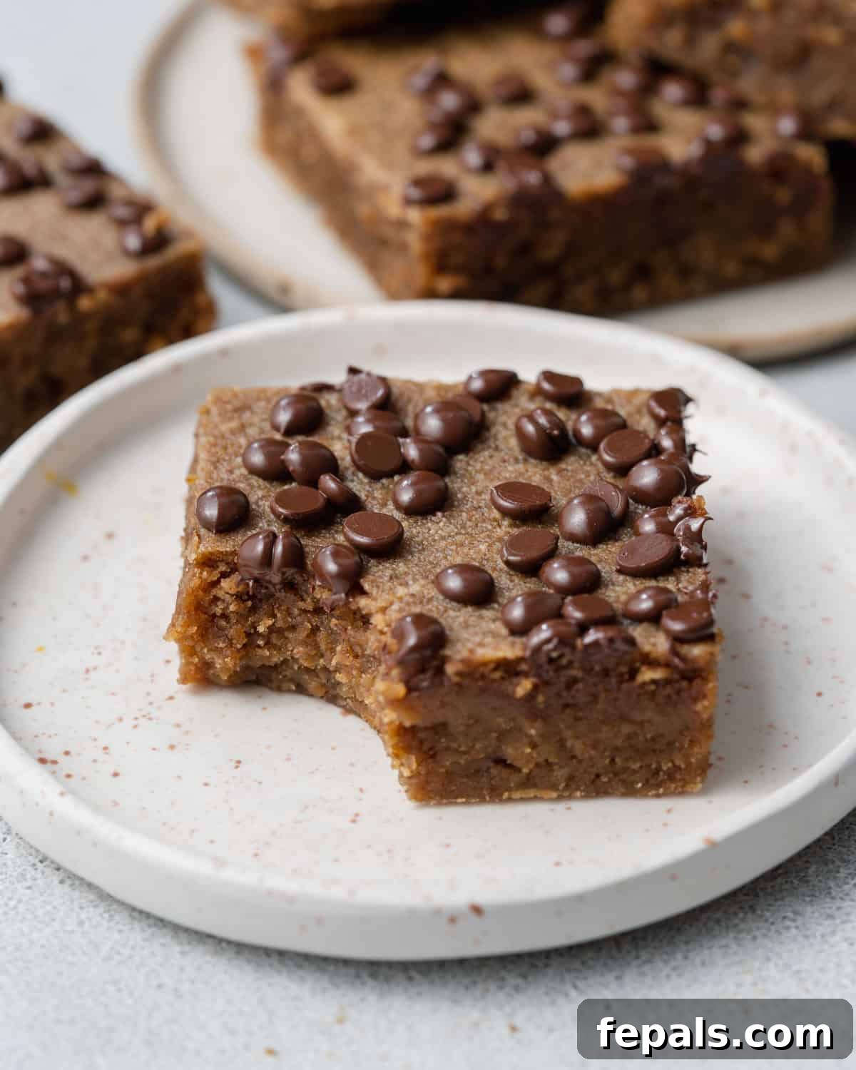 A single square paleo pumpkin bar on a plate with a bite taken out, revealing its soft and moist interior.