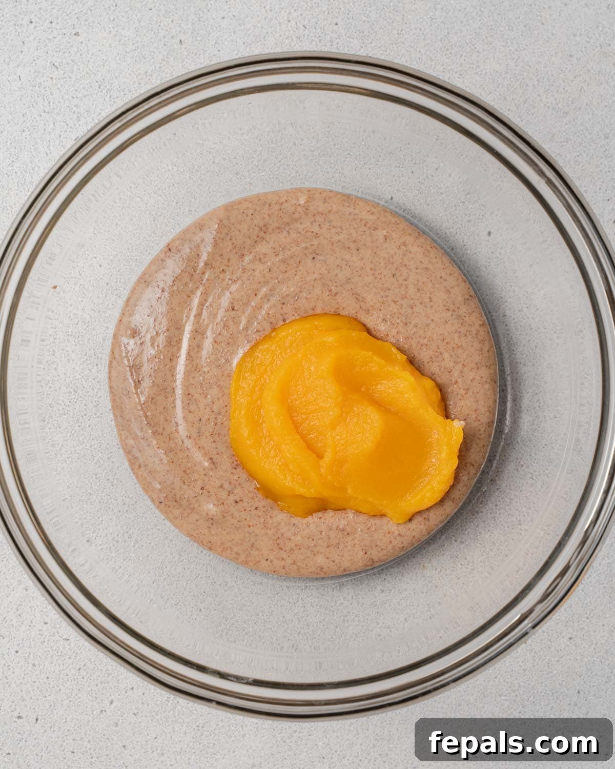 Creamy pumpkin puree being added over smooth almond butter in a mixing bowl.