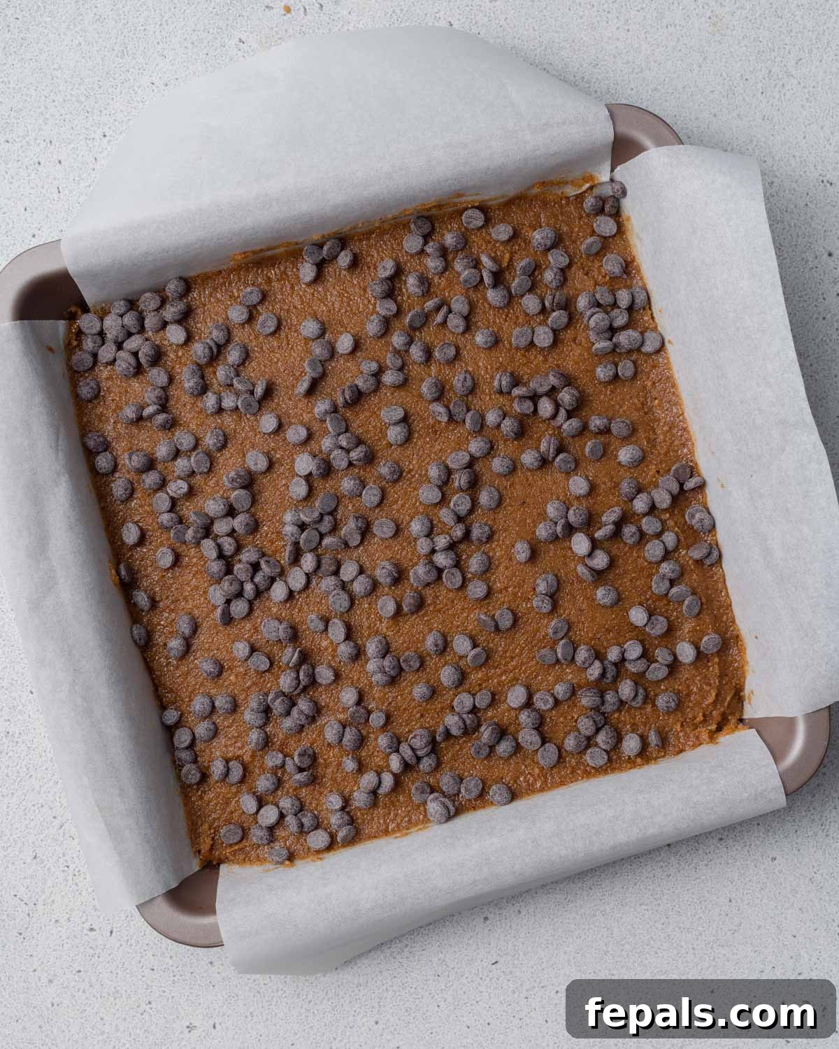Pumpkin batter transferred to a parchment-lined pan and topped with an abundance of dark chocolate chips.