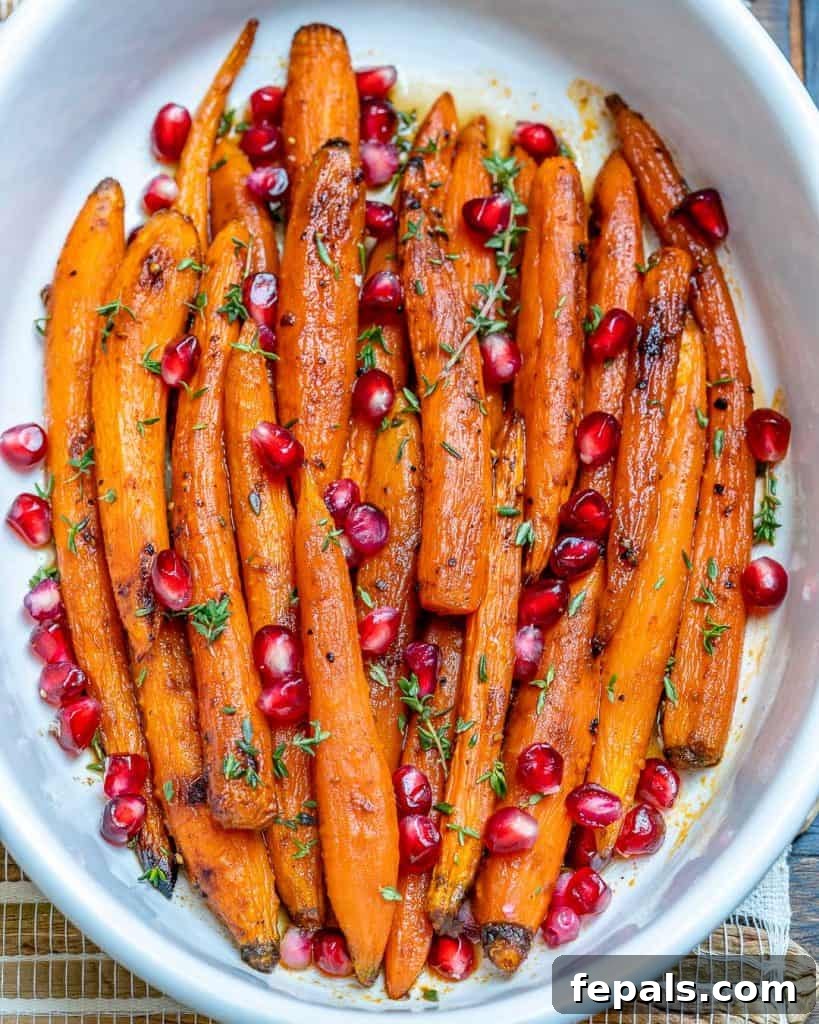 roasted carrots in a white dish topped with pomegranate seeds