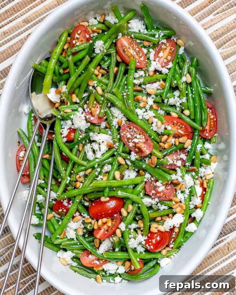 Sun-Kissed Tomato and Crisp Green Bean Salad 2 Top view of a vibrant green bean salad in a white bowl, garnished with crumbled feta cheese and bright cherry tomatoes, ready to be served.