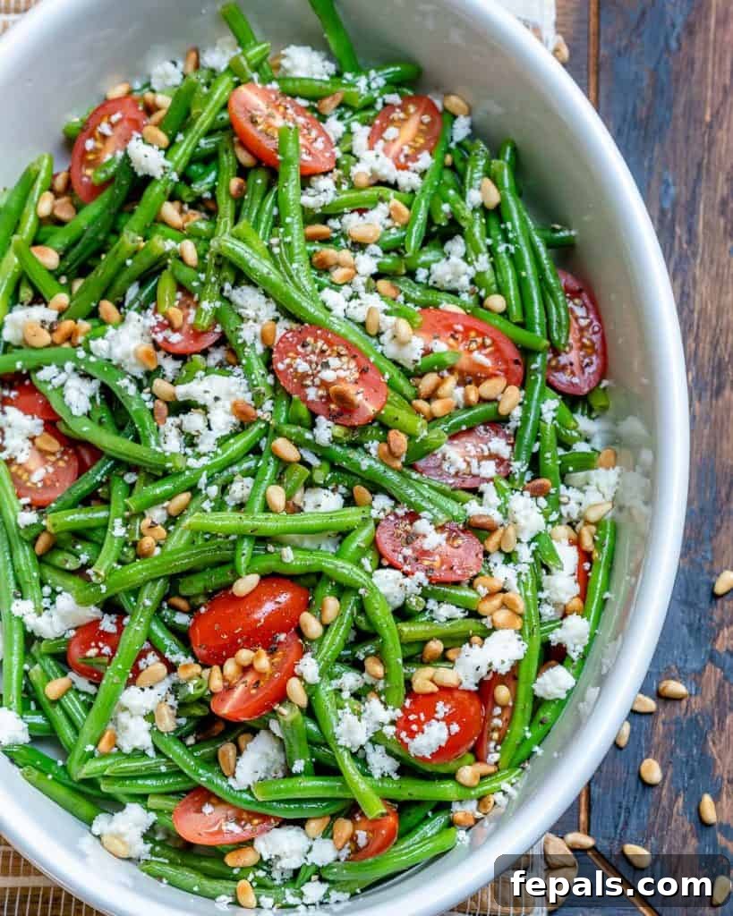 Sun-Kissed Tomato and Crisp Green Bean Salad 5 A detailed top view of the green bean and tomato salad, highlighting the golden-brown toasted pine nuts and crumbled feta cheese atop the vibrant green beans.
