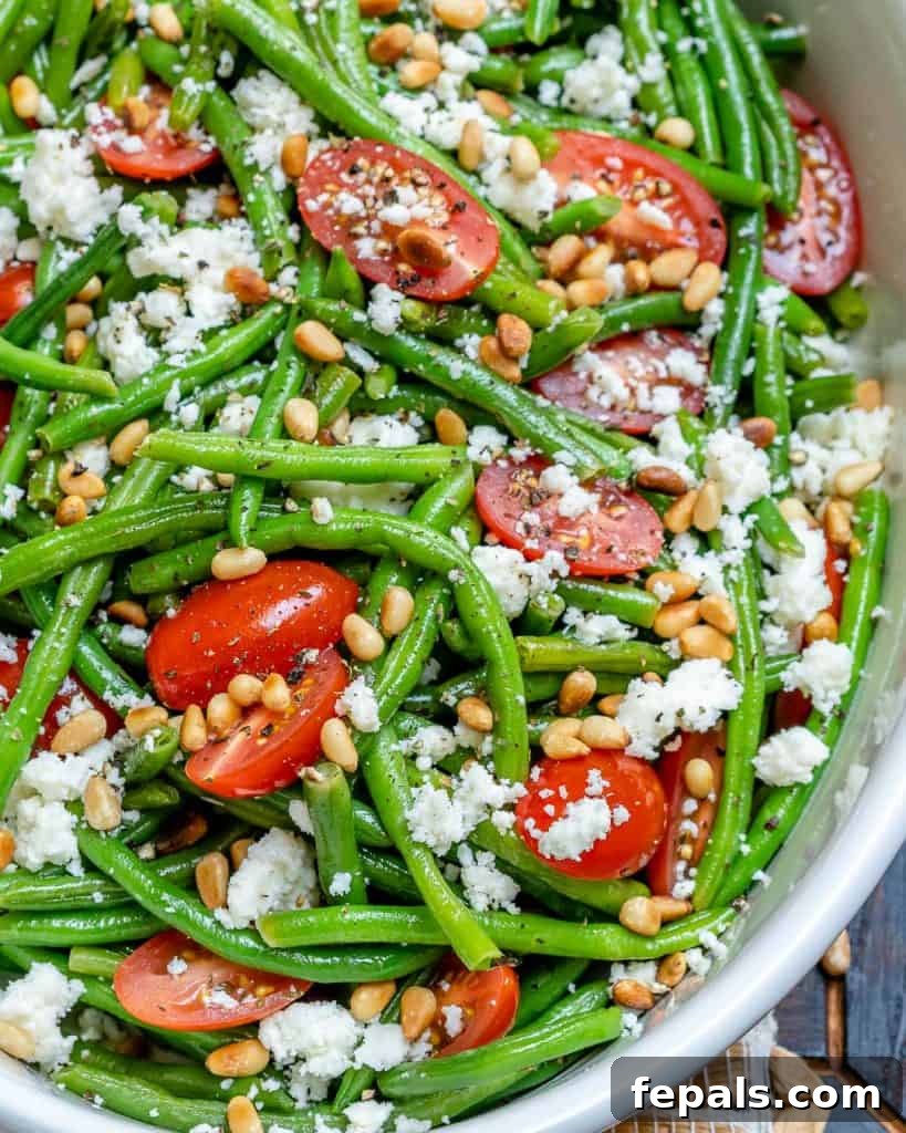 Sun-Kissed Tomato and Crisp Green Bean Salad 7 A close-up image of the green bean and tomato salad served in a white bowl, generously topped with toasted pine nuts and creamy feta cheese, highlighting its appealing presentation.