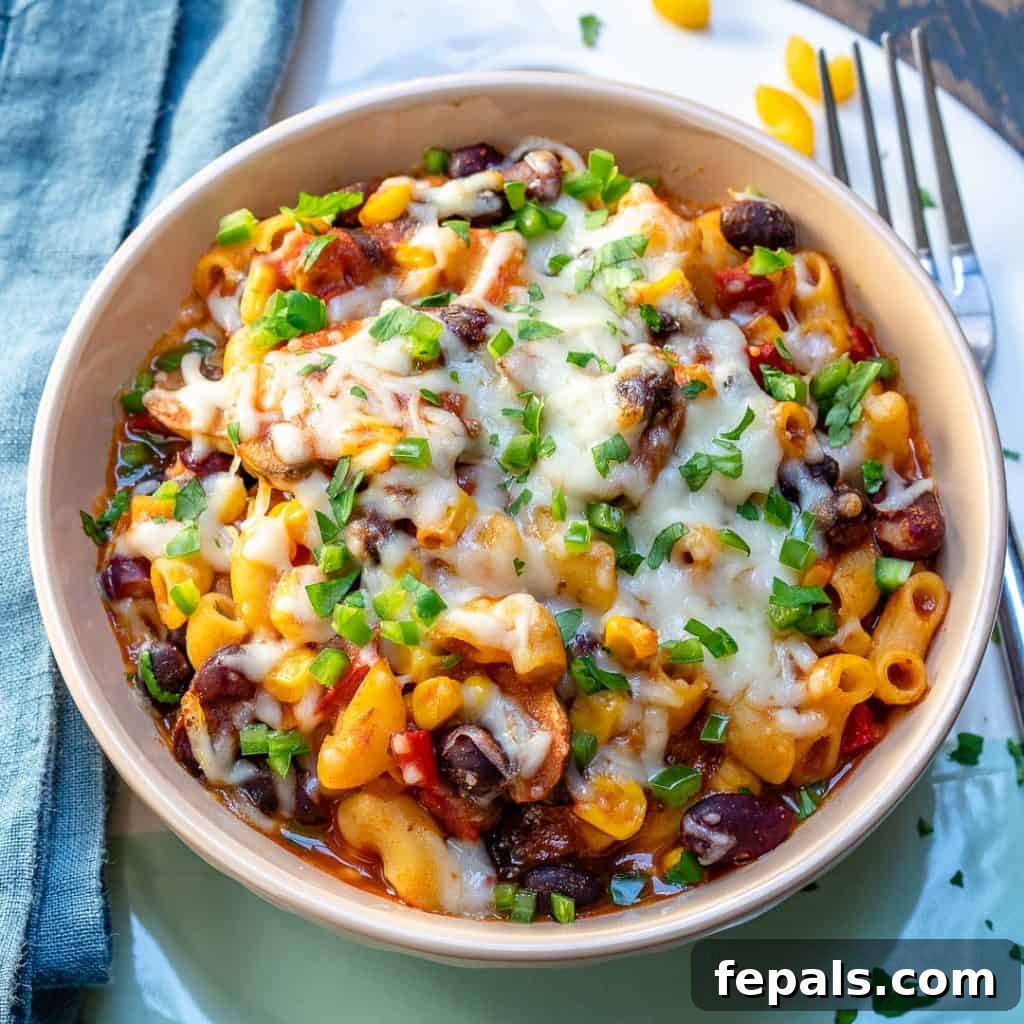 A side shot of a bowl of chili mac and cheese recipe with a fork resting on the right side, inviting viewers to take a bite.