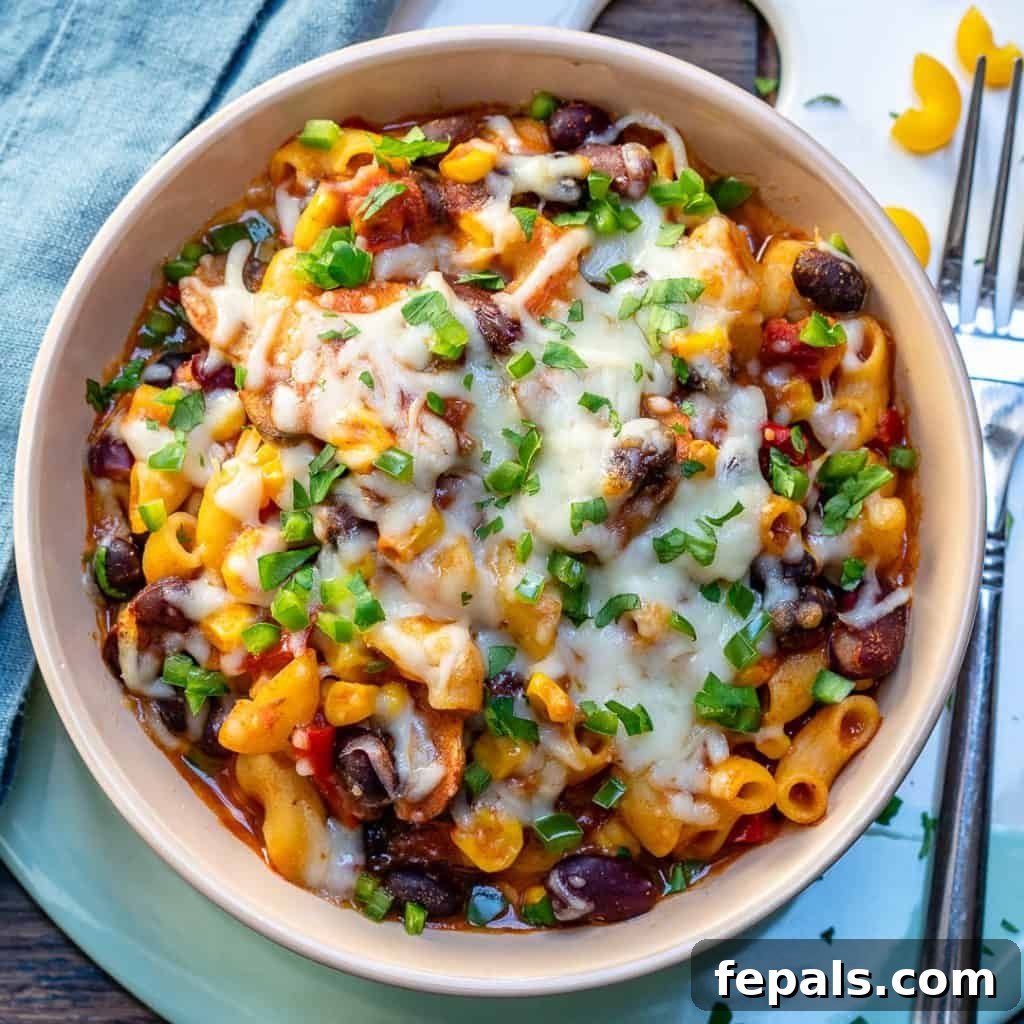A close-up of a bowl of chili mac and cheese, with a fork on the right, highlighting the rich texture and melty cheese.
