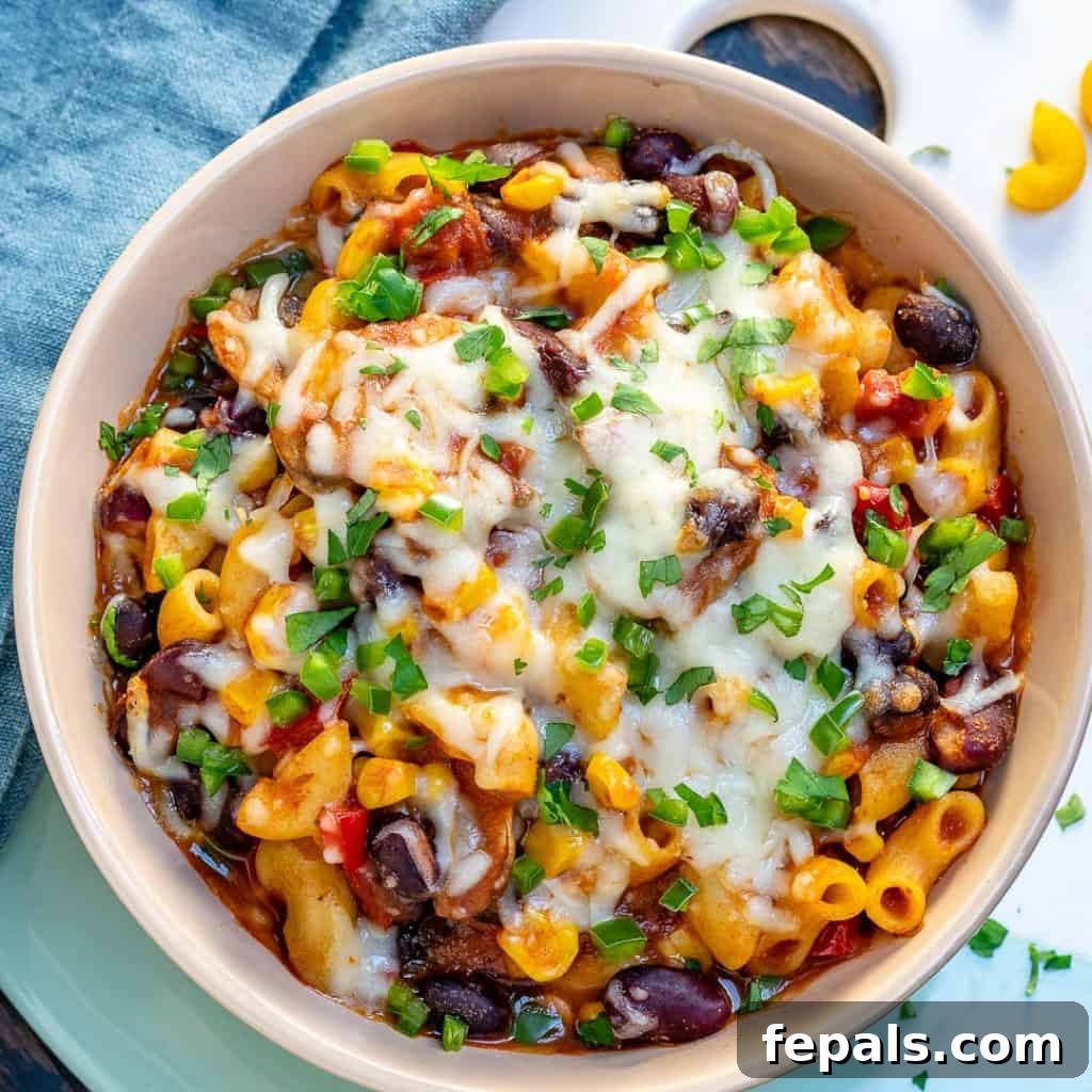 A top-down view of a round bowl of mac and cheese chili recipe generously topped with melted cheese, creating a gooey and inviting appearance.