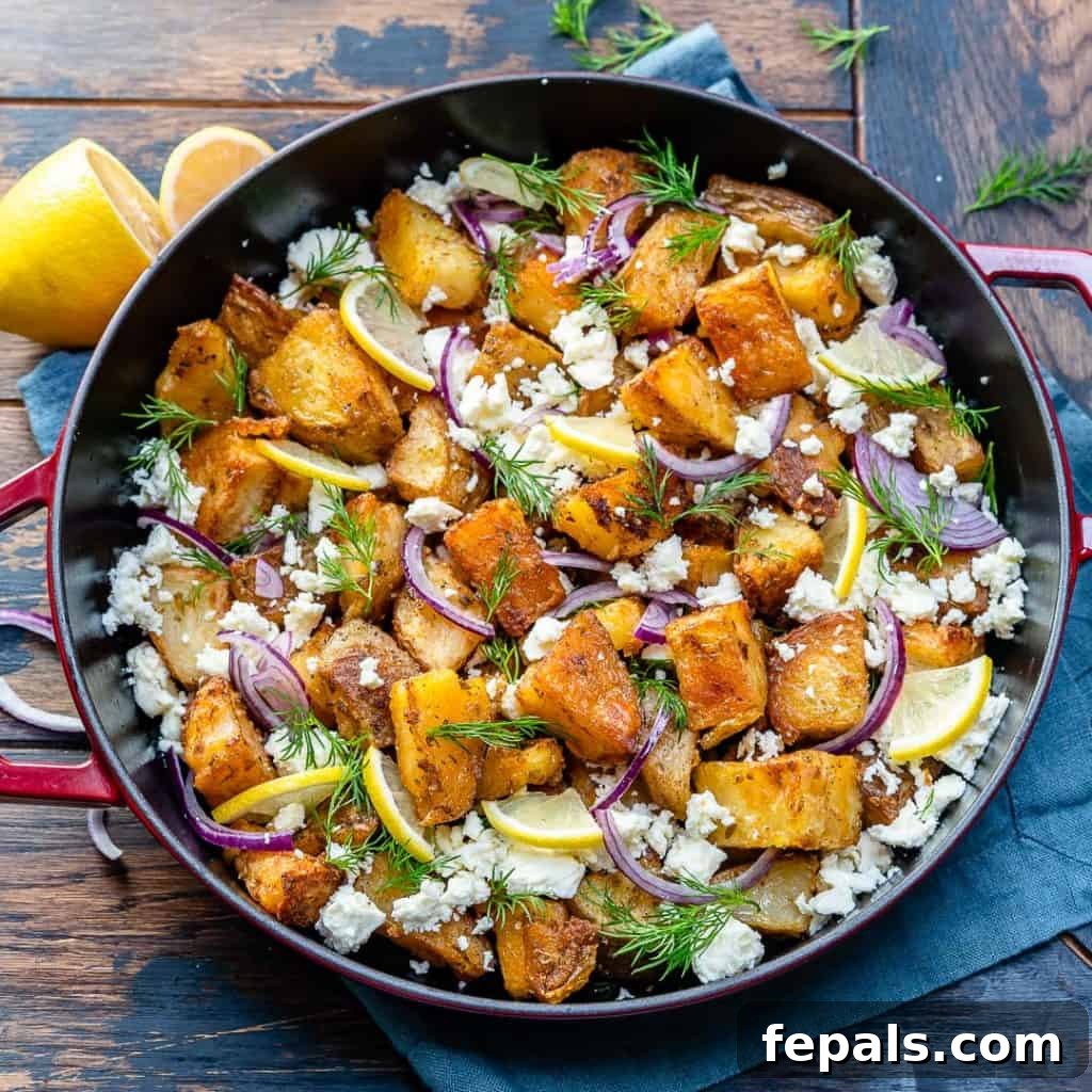 Zesty Greek Roasted Potatoes 10 skillet full of crispy potatoes topped with crumbled feta, lemon wedges, chopped fresh dill, and sliced red onions