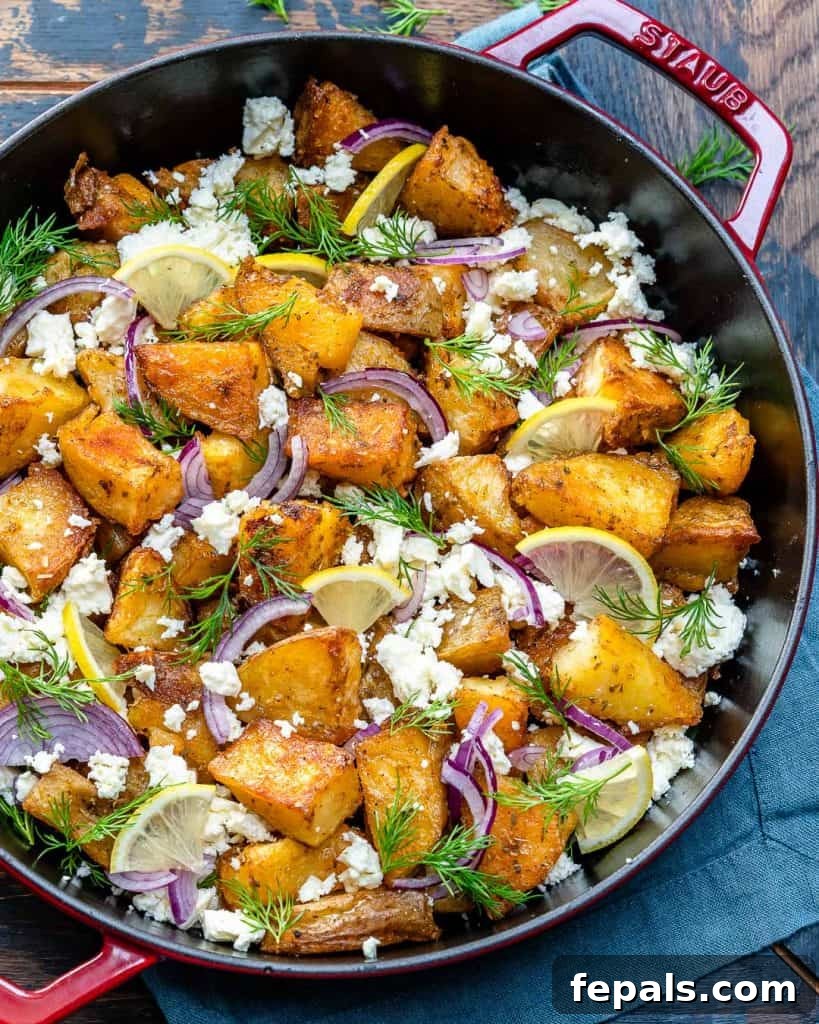 Zesty Greek Roasted Potatoes 4 top view of a black and red skillet with crispy potatoes and style garnishes like crumbled feta, lemon, dill, and onion