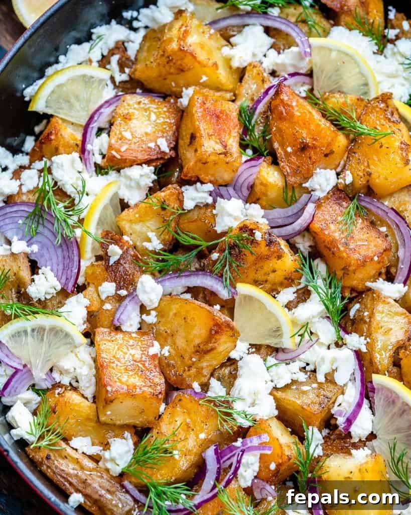 Zesty Greek Roasted Potatoes 8 top-down shot of crispy looking potatoes topped with crumbled feta, sliced purple onions, sliced lemons, and chopped fill