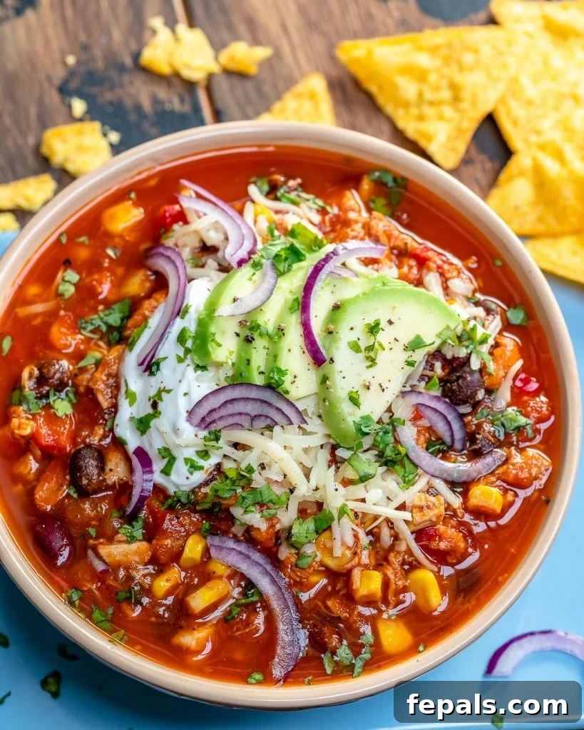 Ultimate Chicken Chili 3 top view of a bowl of red chili with chicken beans and corn, topped with sliced avocado, sour cream, and shredded cheese