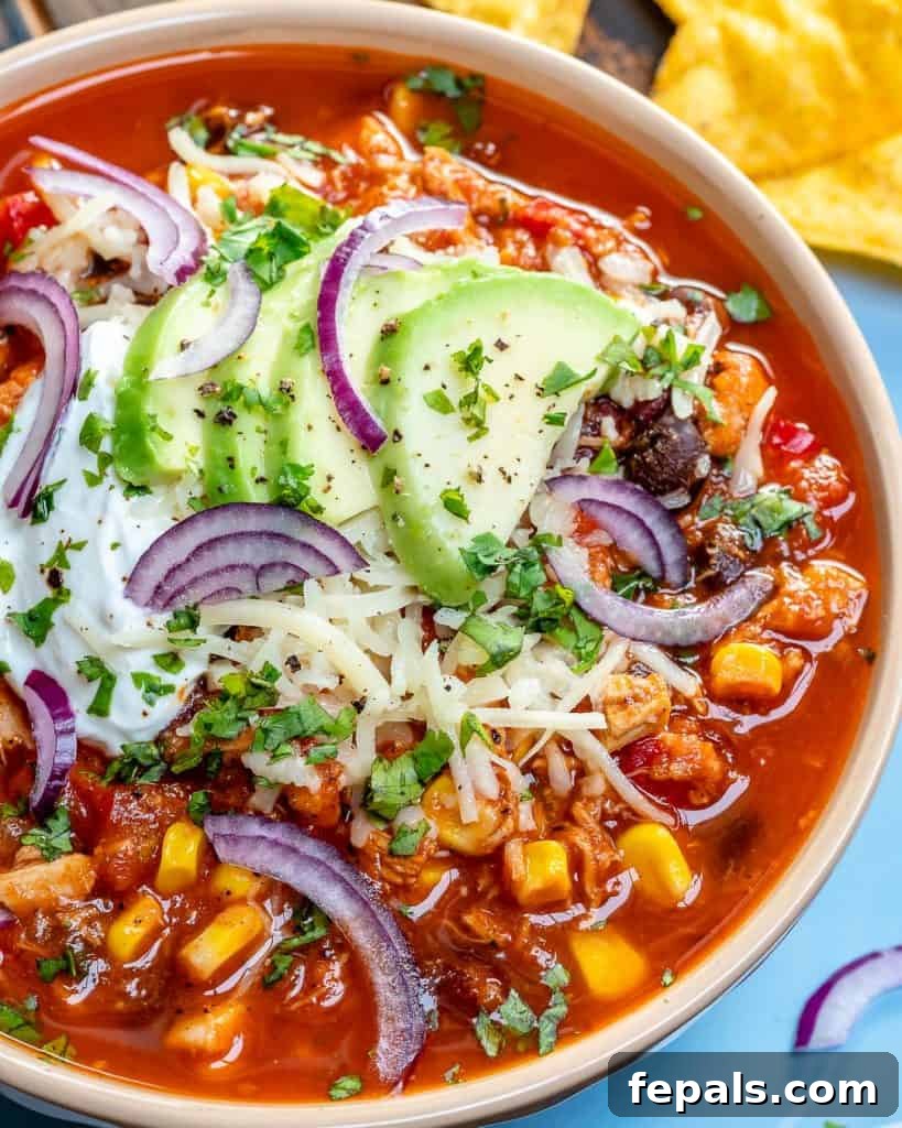 Ultimate Chicken Chili 5 close up image os a bowl of chicken chili with black beans, corn, and chicken, topped with sliced onions, sliced avocado and shredded cheese