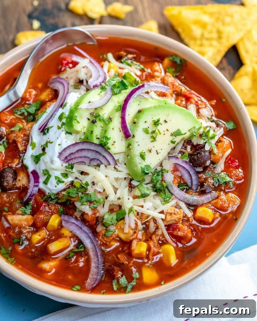 Ultimate Chicken Chili 6 a bowl of chili soup that's red in color made with black beans, chiken, corn, and garnished with shredded cheese avocado, and sour cream