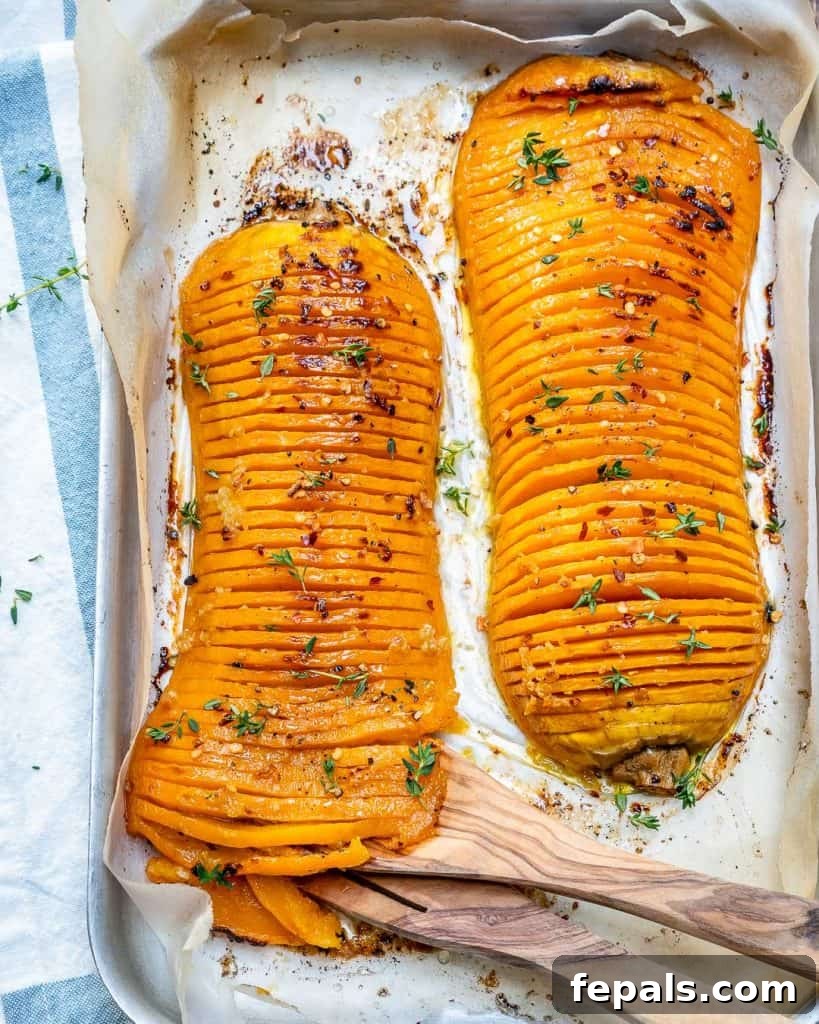 Two halves of Hasselback butternut squash on a baking sheet, glistening with glaze.