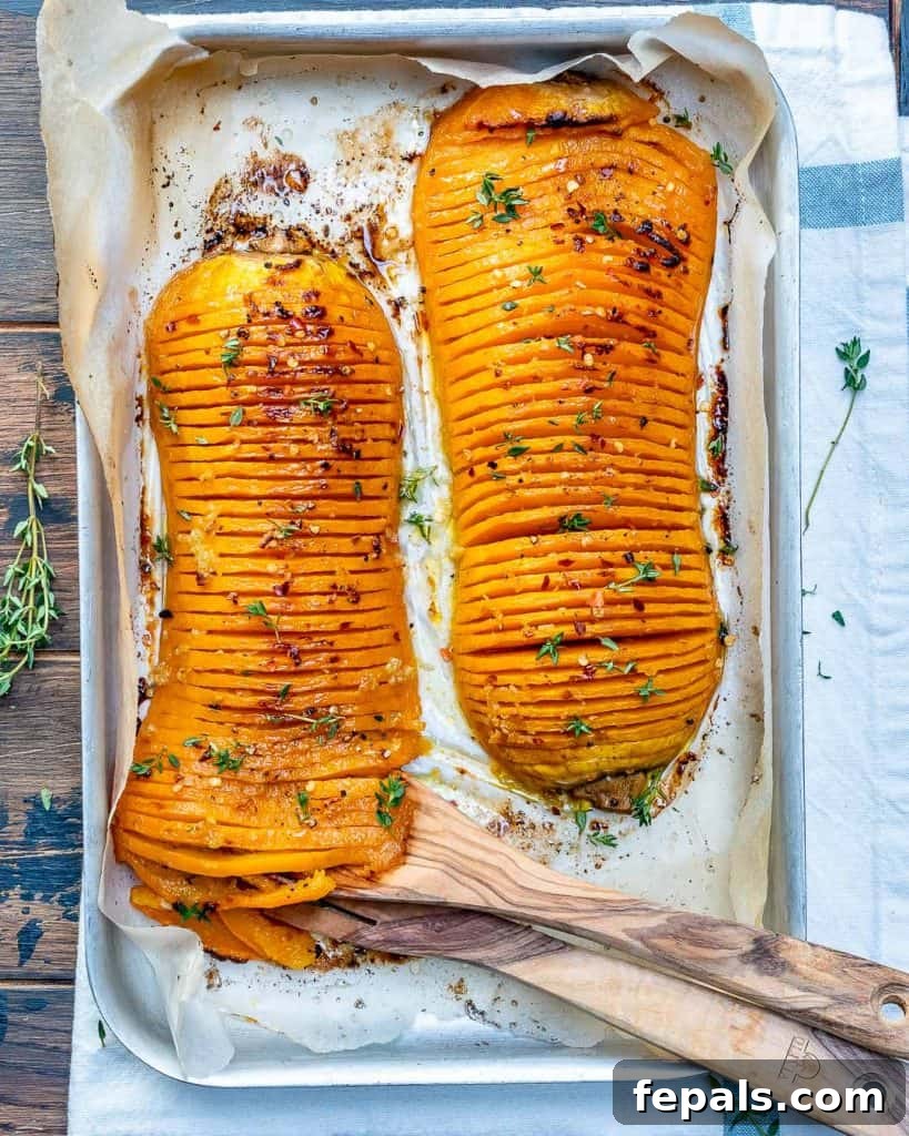 Top view of two Hasselback butternut squash on a baking pan with a wooden spoon, ready to be served.