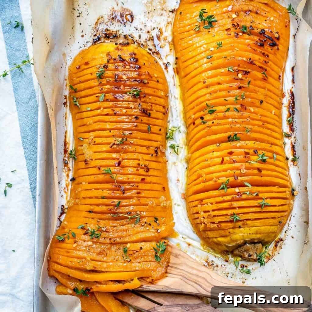 Top view of two Hasselback butternut squash halves on a baking pan with garnishes.