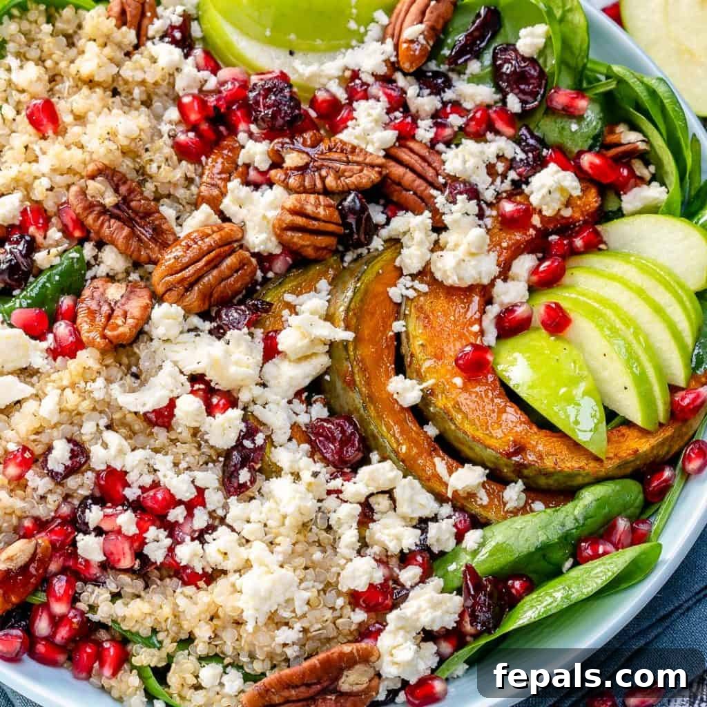 close up image of a salad bowl brimming with quinoa, fresh spinach, apple slices, crumbled feta, and vibrant pomegranate seeds
