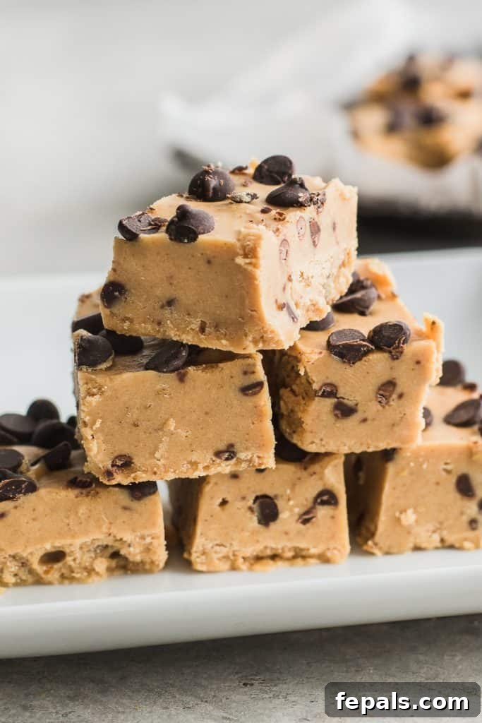 Effortless Chocolate Chip Cookie Dough Fudge 6 Side view of a perfectly square piece of cookie dough fudge resting on a white surface, highlighting its thickness and uniform texture.