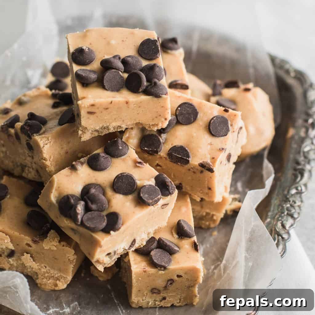 Effortless Chocolate Chip Cookie Dough Fudge 8 A container filled with freshly made chocolate chip cookie dough fudge squares, neatly arranged with parchment paper.