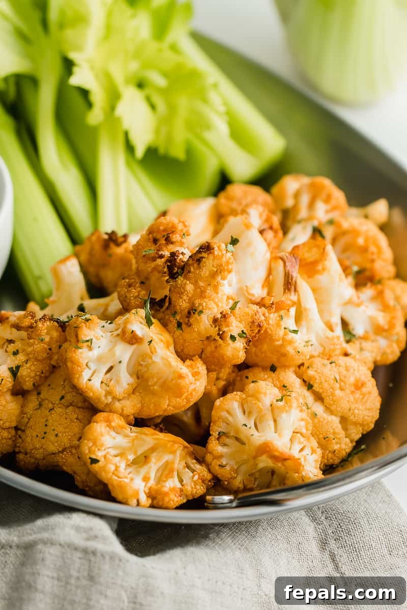 Healthy Buffalo Cauliflower Bites Roasted cauliflower coated in buffalo sauce, served with celery sticks on a dark plate, indicating a healthy and flavorful appetizer.