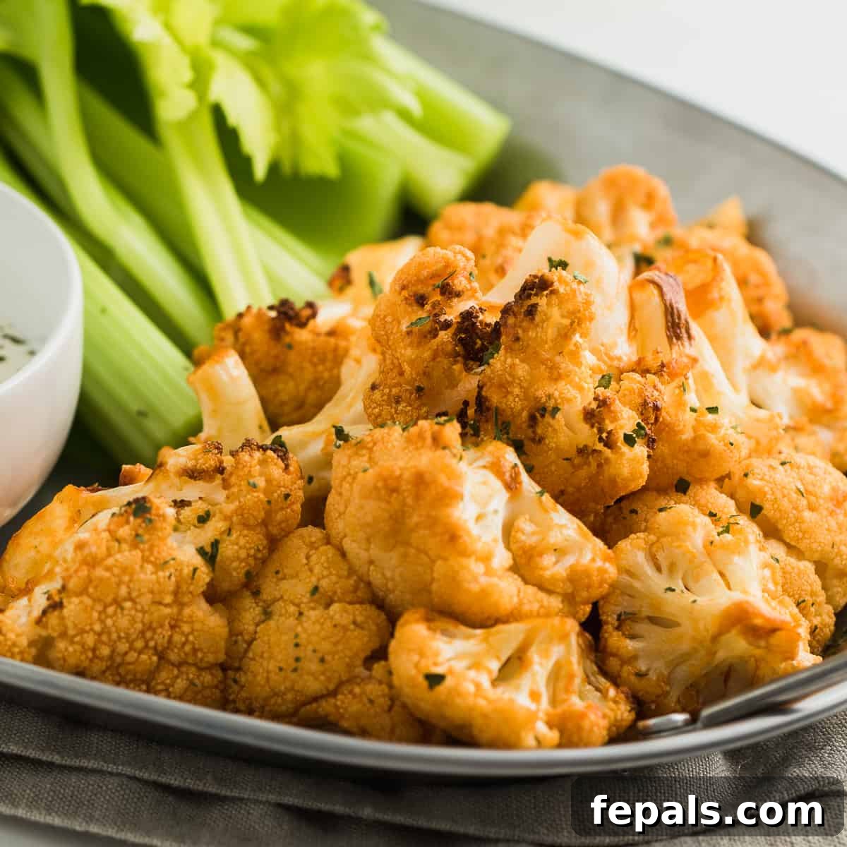 Healthy Buffalo Cauliflower Bites Buffalo Cauliflower bites arranged on a plate with fresh celery sticks and a bowl of dipping sauce, showcasing a complete appetizer serving.