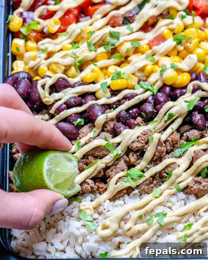 Beef Burrito Power Bowls 5 close up shot of a beef burrito bowl with layer of cream sauce and a hand holding a lime wedge squeezing lime into the bowl