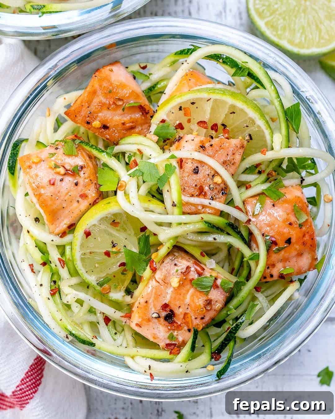 Meal Prep Chili Salmon and Zoodles Top-down view of a beautifully arranged easy salmon recipe with zucchini noodles, garnished with fresh herbs, in a glass meal prep container.