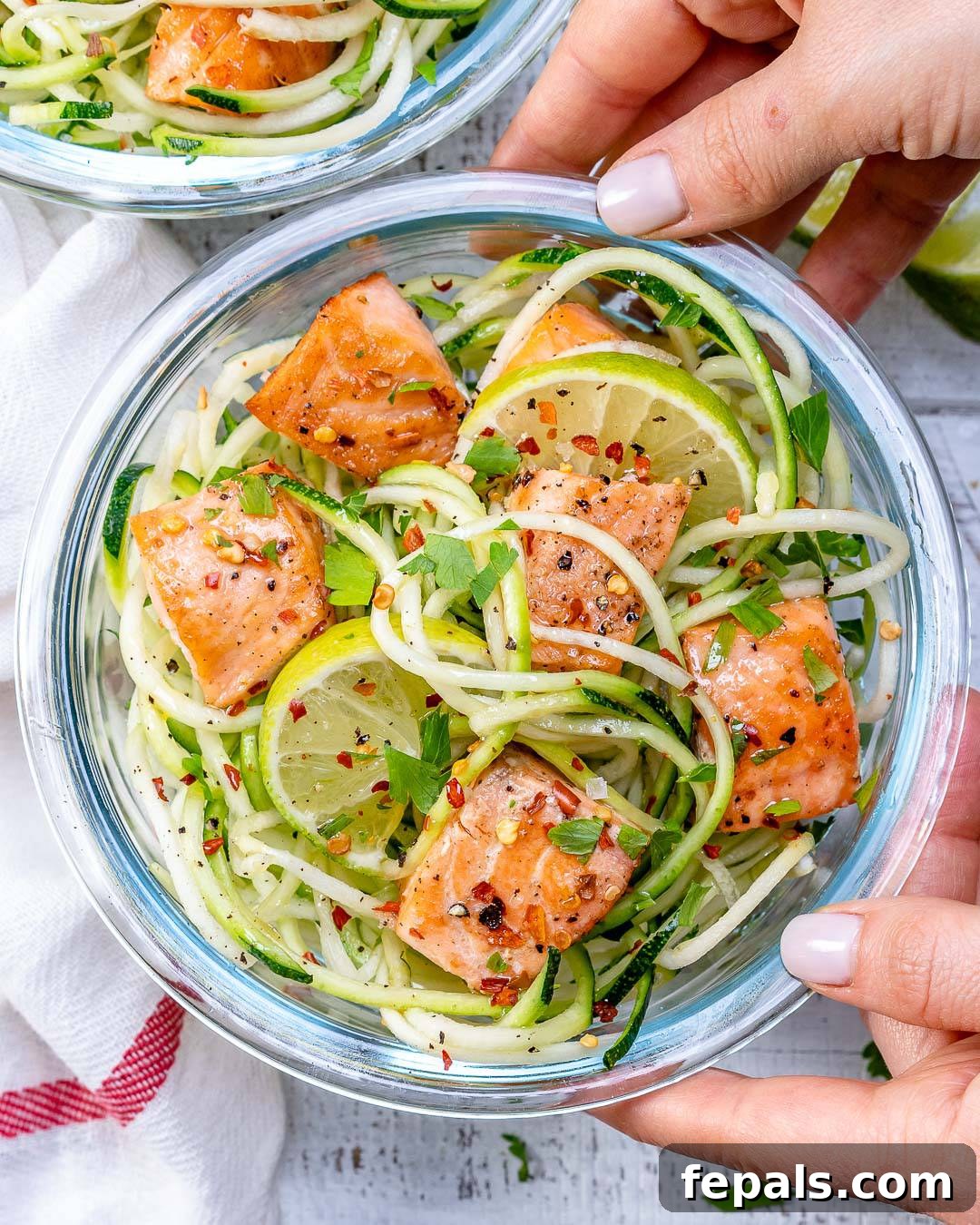 Zesty Chili Salmon Zoodles 3 Hand holding a glass container filled with chili lime salmon bites and zucchini noodles, showing a generous serving.