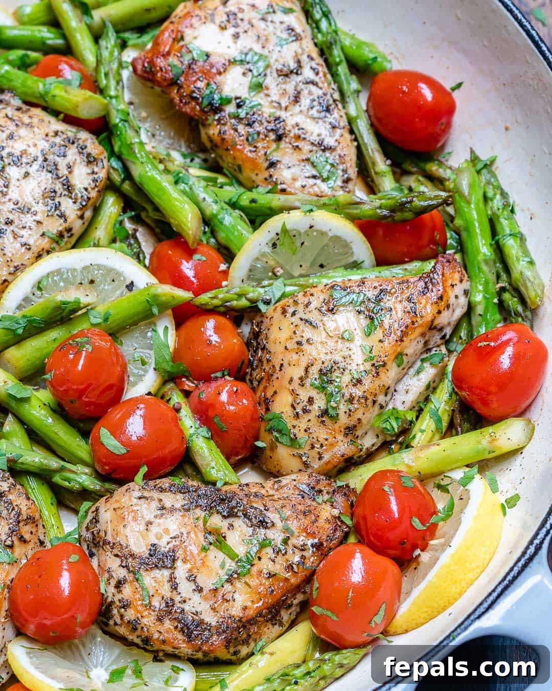Seared Garlic Chicken Perfection 2 Golden-brown pan-seared garlic chicken breast cooking in a skillet alongside fresh green asparagus and bright red cherry tomatoes, garnished with fresh herbs.