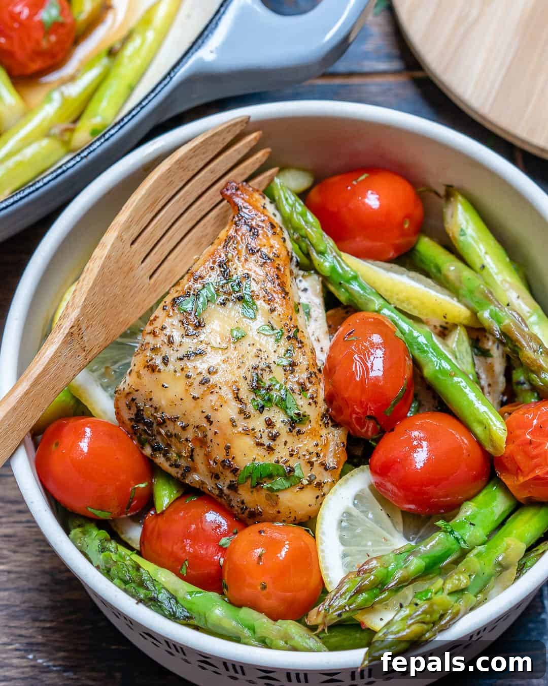 Seared Garlic Chicken Perfection 5 A close-up of a single serving of cooked chicken breast, asparagus, and cherry tomatoes in a white bowl, garnished with fresh parsley.