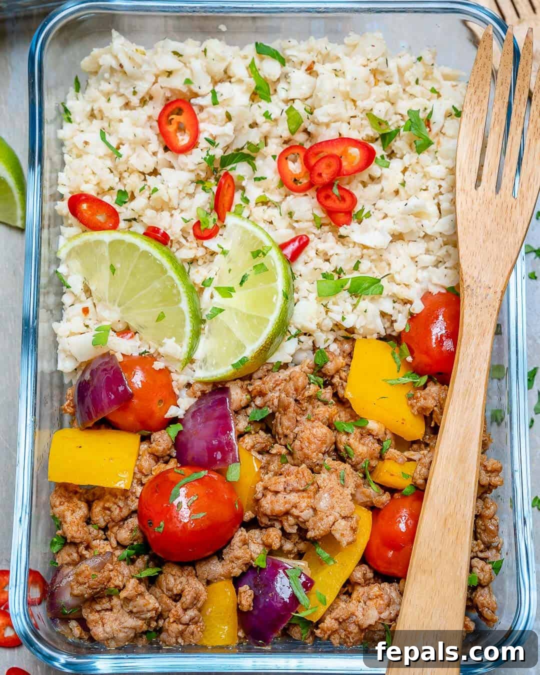 Ground Turkey and Cauliflower Rice Skillet Ground turkey recipe in a glass container with cauliflower rice, lime, and various veggies, highlighting fresh ingredients.