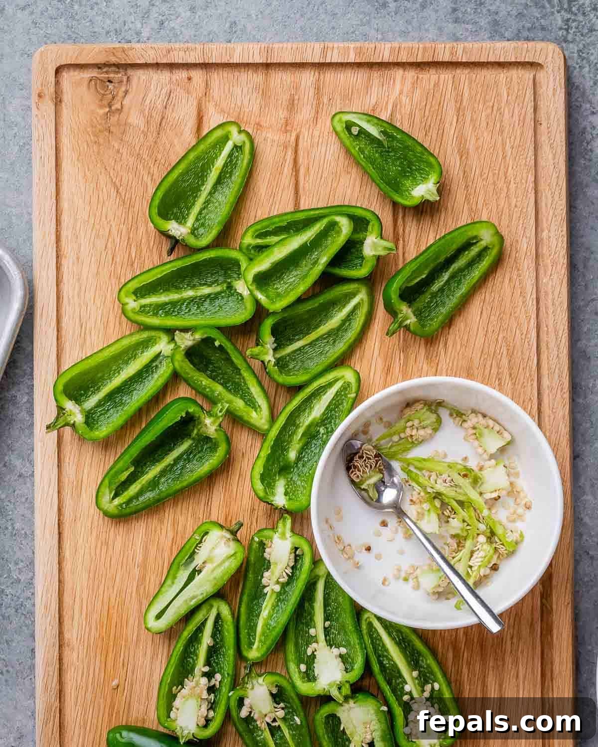 Fresh jalapenos are neatly sliced in half lengthwise and deseeded, resting on a cutting board, ready for stuffing.