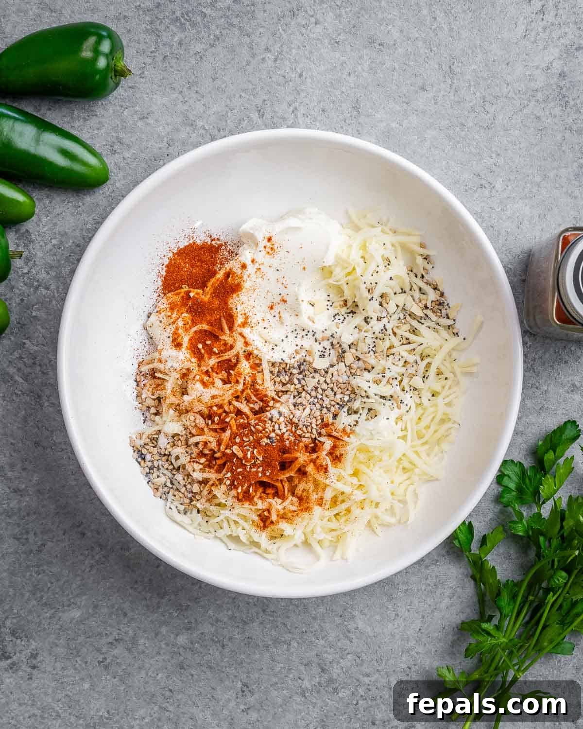 A mix of cream cheese, shredded cheddar, and various seasonings are placed together in a bowl, ready to be combined into a creamy stuffing for jalapeno poppers.