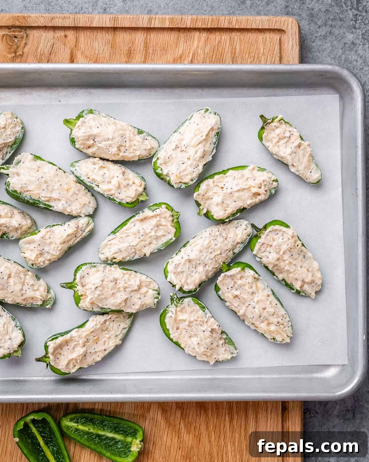 Stuffed jalapeno halves, generously filled with a creamy cheese mixture, are neatly arranged on a parchment-lined sheet pan, ready for baking.