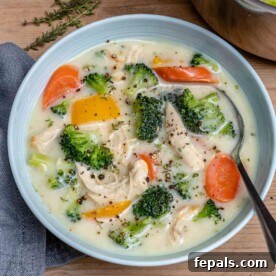 top view os a white bowl of creamy white looking chicken soup with broccoli, yellow peppers, and carrots