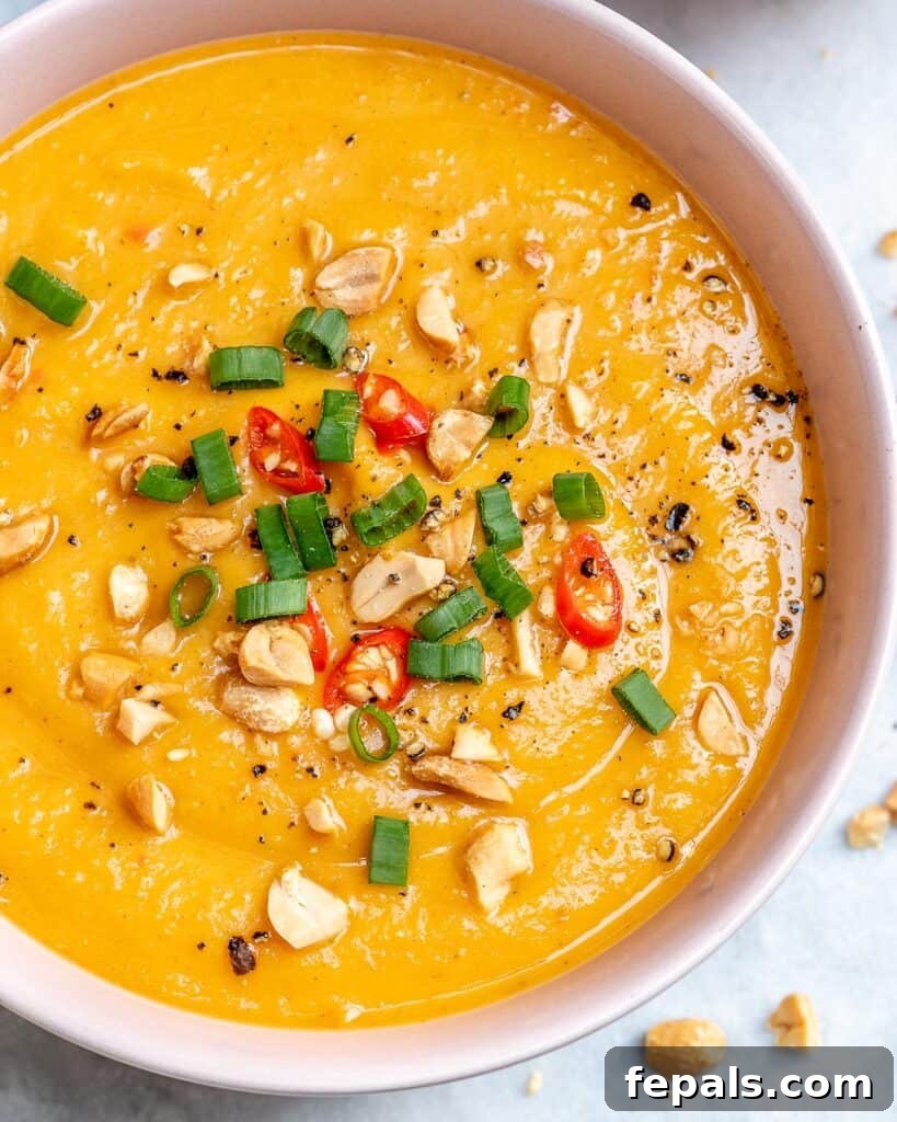 overhead shot of Sweet Potato Soup in a round white bowl topped with fresh peanuts green onions and sliced chili peppers.