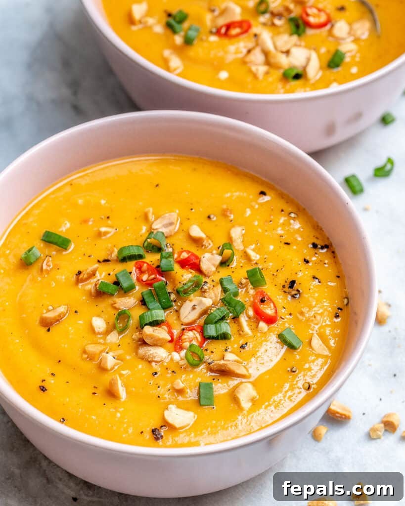 two white bowls of sweet potato soup thats orange in color and topped with peanuts, green onions, and chili peppers 