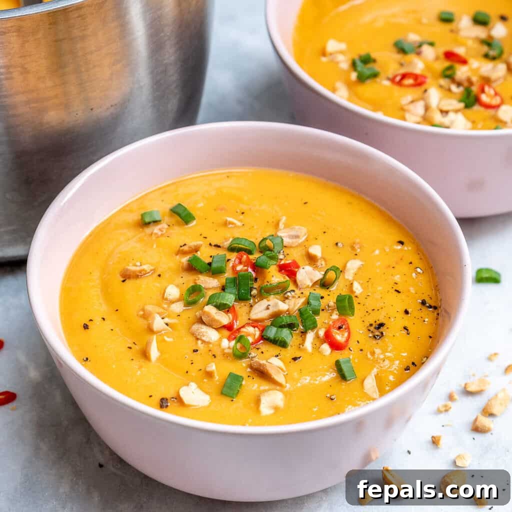 side shot of a white bowl that has blended sweet potato soup, topped with peanuts, sliced green onions, and slice red chili peppers