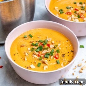side shot of a white bowl that has blended sweet potato soup, topped with peanuts, sliced green onions, and slice red chili peppers