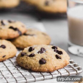 A perfectly baked keto chocolate chip cookie on a wire rack, with a glass of milk in the background, ready to be enjoyed.