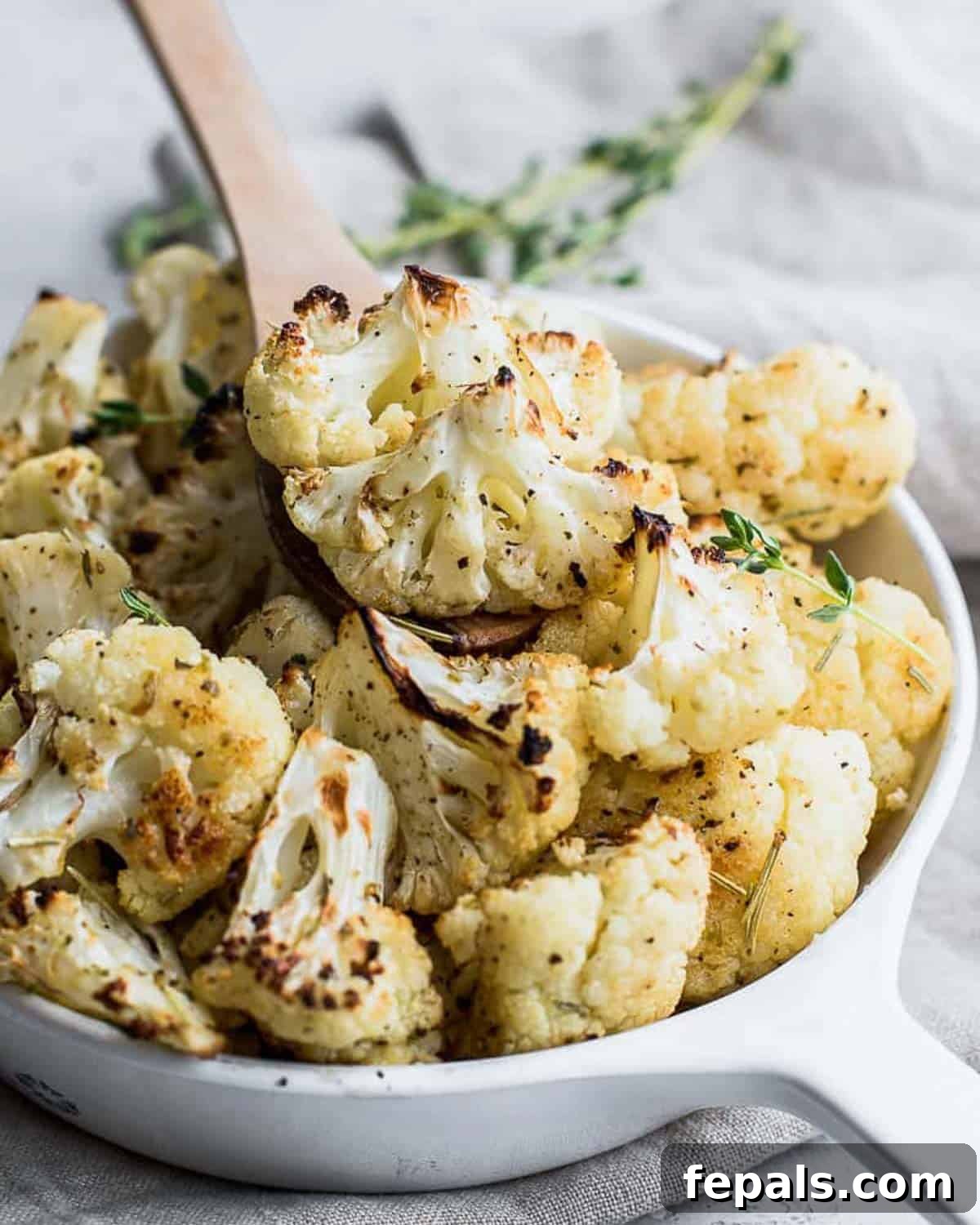 Close-up view of roasted cauliflower florets seasoned with garlic and herbs, presented in a rustic bowl.