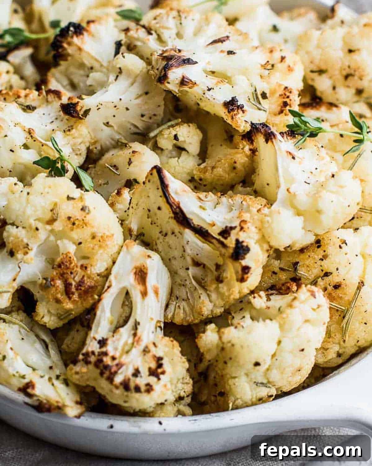 A vibrant bowl of roasted cauliflower, golden-brown and perfectly seasoned with garlic and Italian herbs.