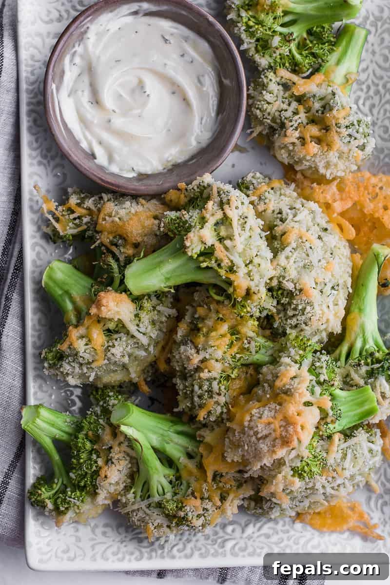 Baked broccoli on a plate with a side of dipping sauce, highlighting its crispy texture.