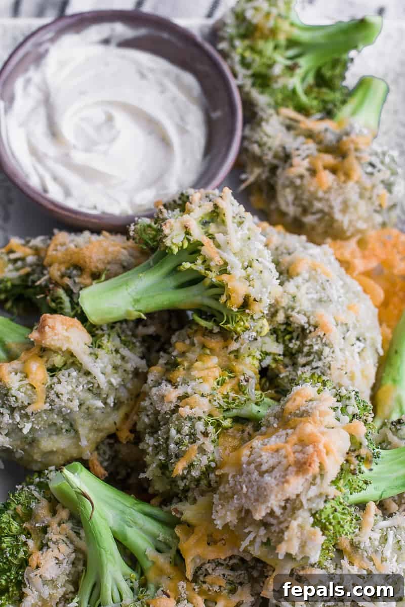 Top view of a serving plate filled with baked broccoli and a small bowl of creamy white dipping sauce.